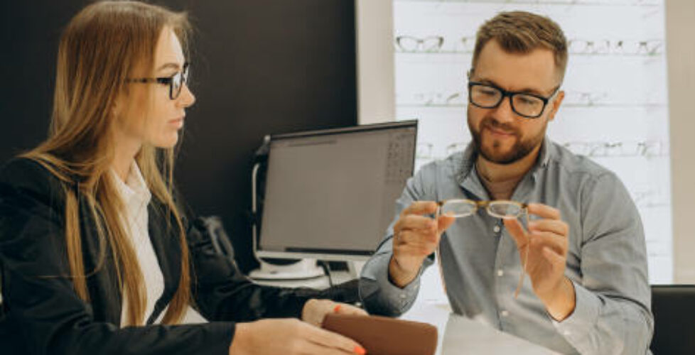 Customer shoosing spectacles at optic store with the lelp of sales person